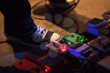Foot of guitar player on a stage with set of distortion effect pedals. Closeup photo with selective focus
