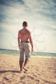 Barefoot sporty man goes on sandy summer beach to the sea, colorful tonal filter correction, vintage stylized photo with old style effect