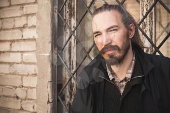 Outdoor portrait of young bearded Asian man in black on gray urban grungy brick wall background, vintage stylized photo with warm tonal correction photo filter