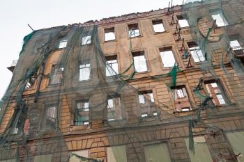 Old living house is under reconstruction, facade with empty windows is covered with green protection mesh