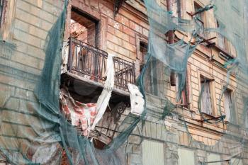 Old living house is under reconstruction, facade with broken balcony is covered with green protection mesh