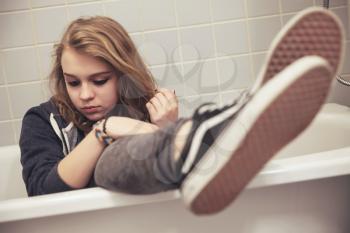 Teenage girl in black sporty sneakers sits in white bath. Closeup photo with selective focus on face, tonal filter correction, vintage stylized