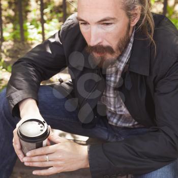 Bearded Asian man with coffee in paper cup, outdoor square portrait with selective focus