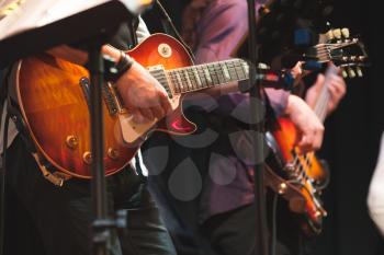 Rock and roll music background, guitar players on a stage with colorful illumination, selective focus