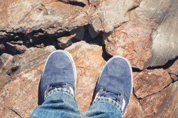 Male feet in blue canvas sport shoes standing on rough rocky ground