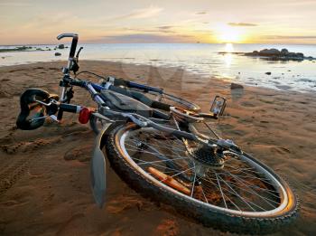 At the end of a journey. Bicycle lying on the beach in the light of setting Sun