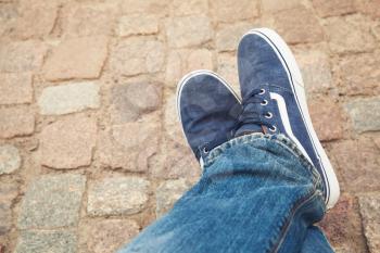 Relaxing male feet in blue canvas sporty shoes on old rough stone pavement
