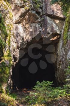 Entrance to dark cave in the rock, vertical photo