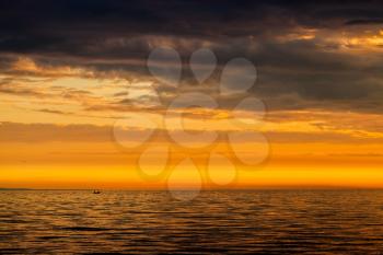 Dramatic cloudscape, bright sunset over Baltic Sea. Cloudy sky, still water and fishermen on a small boat in the distance