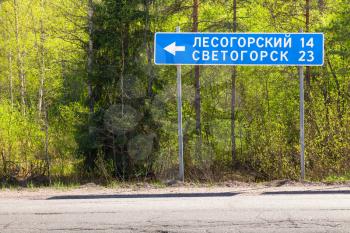 Blue road sign near highway with the names of settlements and the distance to them. Russian text means Lesogorsky and Svetogorsk towns
