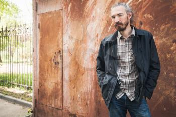 Outdoor portrait of young bearded Asian man in casual clothes over rusted grungy garage wall background