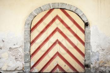 Ancient wooden door with red striped pattern in yellow stone wall. Tallinn, Estonia