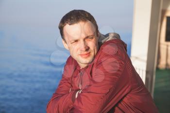 Young handsome Caucasian man standing on the walking deck of cruise ship in bright evening sunlight