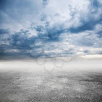 Gray empty asphalt road goes in fog under dramatic cloudy sky, square background photo texture