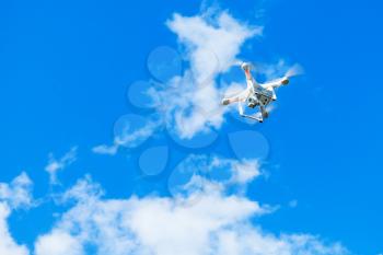 White quadrocopter in blue cloudy sky, drone controlled by wireless remote