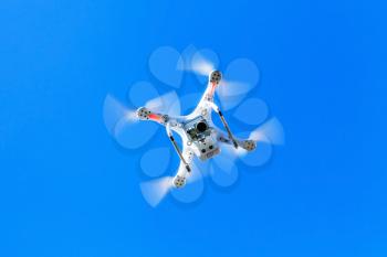 White quadrocopter in blue sky, drone controlled by wireless remote
