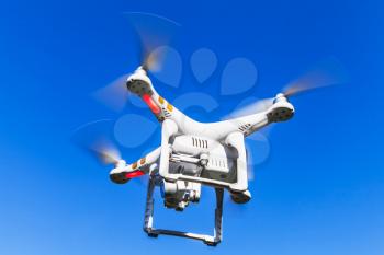 White quadrocopter flying in blue sky, closeup photo of a drone controlled by wireless remote