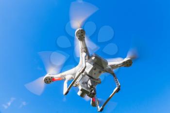 White quadrocopter flying in blue sky, drone controlled by wireless remote