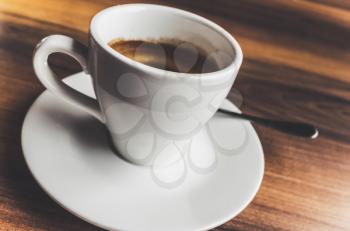 Freshly brewed espresso coffee in white cup on saucer with spoon. Closeup photo with selective focus and vintage tonal correction photo filter, old instagram style effect