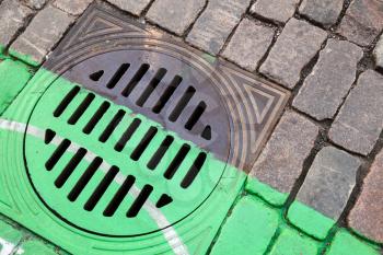 Urban street drainage sewer manhole in cobblestone pavement