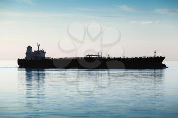 Big industrial tanker ship goes on still sea water, silhouette photo, natural back lit effect