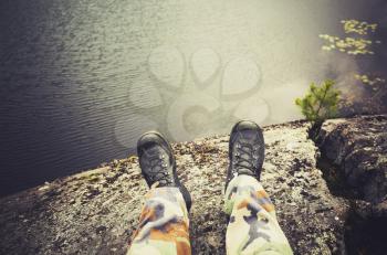 Male feet in camouflage pants and black rough shoes, travel lifestyle background. Vintage tonal correction photo filter, old style effect