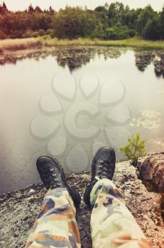 Male feet in camouflage pants and black rough shoes, vertical travel lifestyle background. Vintage tonal correction photo filter, old style effect