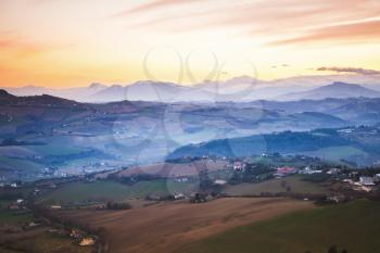Morning panorama of Italian countryside. Province of Fermo, Italy. Villages and fields on hills under colorful cloudy sky