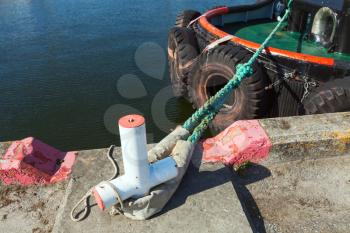 Mooring bollard with green naval rope on concrete pier, tugboat moored in port