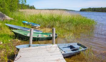 Small rowboats lay on the coast of still lake near wooden pier