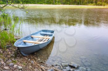 Small blue rowboat lays on coast of still lake