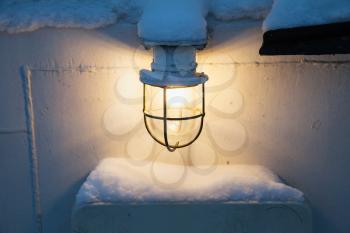 Glowing lamp with warm light on white ship wall in winter