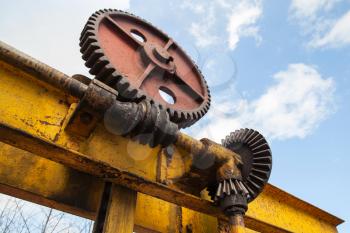 Huge old rusted gears engaged with worm-gear, close up photo with cloudy sky on a background