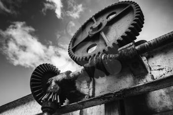 Old rusted gears under dramatic sky background, close-up black and white photo with selective focus