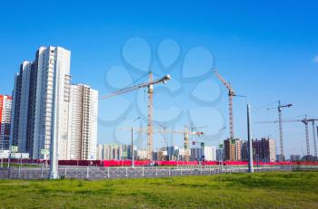 Block of flats under construction, working cranes are under blue sky in summer day