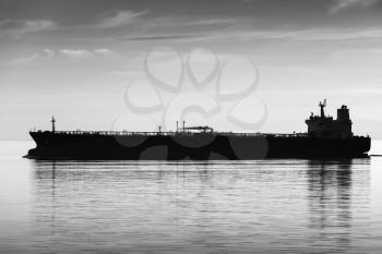 Big industrial tanker ship goes on still sea water, black and white silhouette photo
