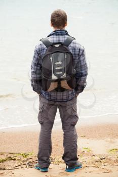 Traveler on Baltic Sea coast. Young adult  Caucasian man in warm outdoor clothes with backpack starring at the sea, rear view
