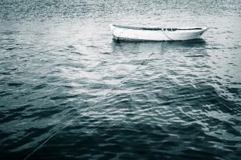 White wooden fishing boat floats on still Sea, blue toned vintage stylized photo
