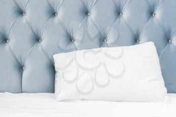 Luxury empty bedroom interior fragment, soft blue headboard, white pillow lays on wide empty bed