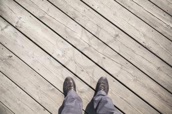 Male feet in leather shoes stand on old wooden pier floor, first person view