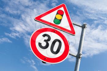 Traffic lights and speed limit 30 km per hour mounted on one metal post. Road signs over blue sky background