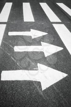 White arrows and stripes over black asphalt road, pedestrian crossing road marking zebra 