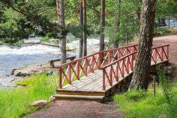 Small wooden bridge with red railings over stream in summer park. Kotka, Finland