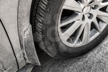 Dirty unidentifiable car wheel with light alloy disc on country road, close up photo