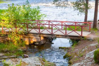 Small wooden bridge with red railings over stream in summer. Kotka, Finland