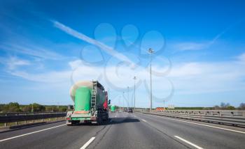 Green cargo tanker truck goes on asphalt highway under blue sky, rear view