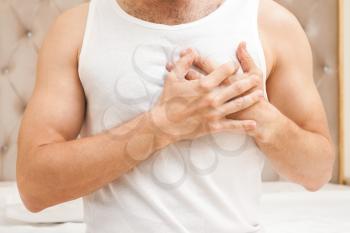 Young sporty Caucasian man in white shirt holds hands near his heart, heart pain gesture