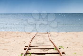 Old rusted railway goes over sandy beach to sea water, useful for boat launching. Photo with selective focus