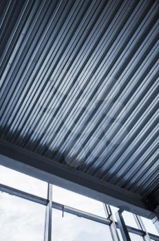 Generic industrial building is under construction. Interior fragment with shining corrugated metal ceiling and empty windows, vertical blue toned photo
