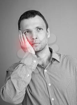 Young Caucasian man with toothache. Black and white stylized photo with red local ache spot